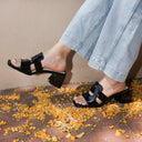 Person wearing black sandals with a platform sole on a sidewalk with autumn leaves.