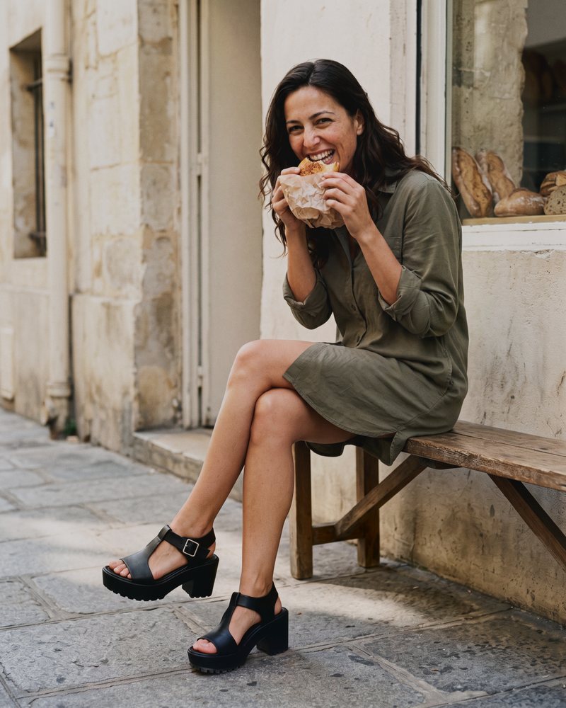 Black and white photo of a woman reading on a Paris station platform bench in black J.Adams Skippy Mary Jane block heels and a wool coat
